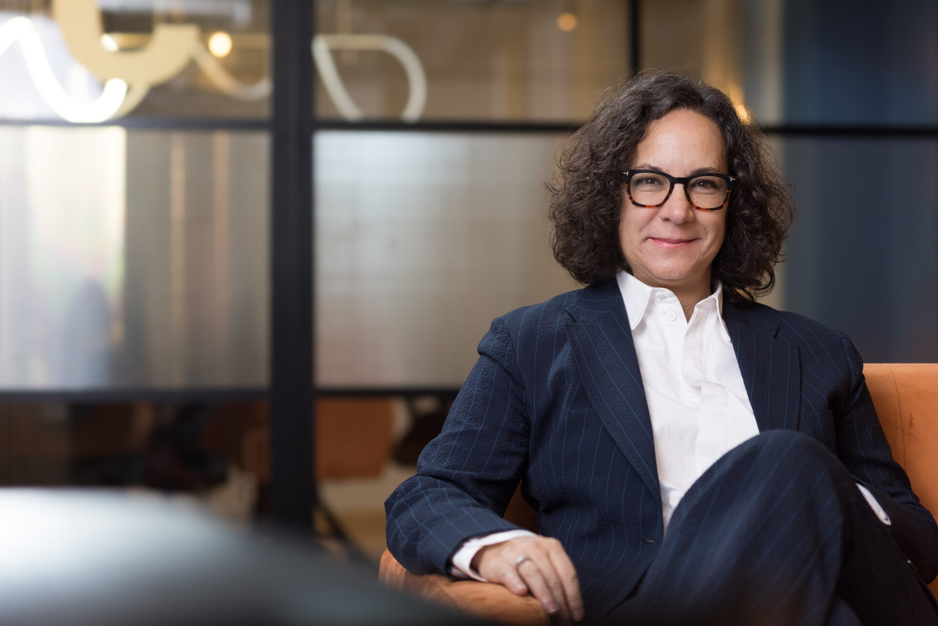 Eva Diego, CEO of Hyphen sitting on an arm chair, looking into the camera and smiling. She is a meeting room.