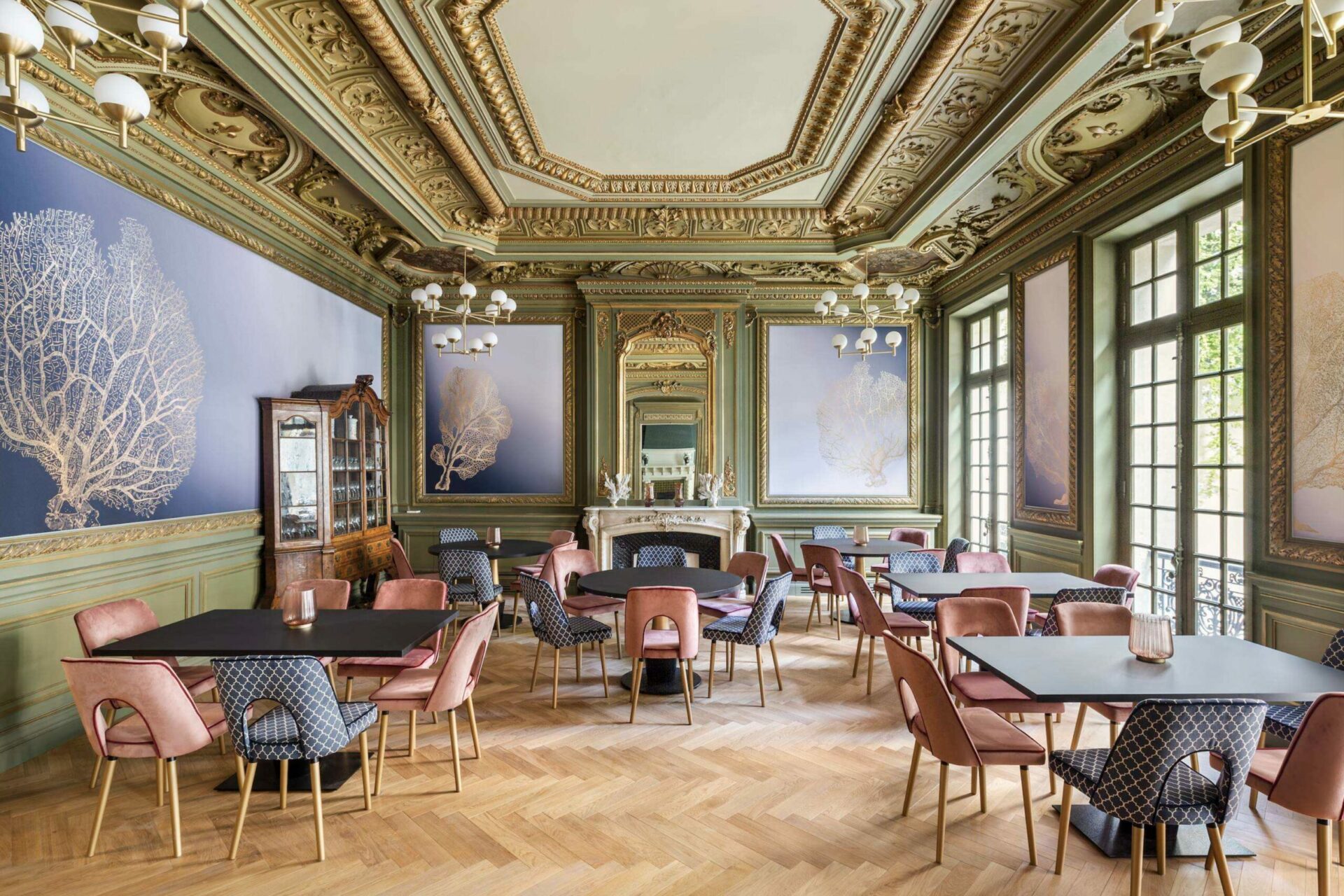 Dining room with an ornate restored ceiling, green wall panelling and tall windows in a converted 19th-century building in Marseille
